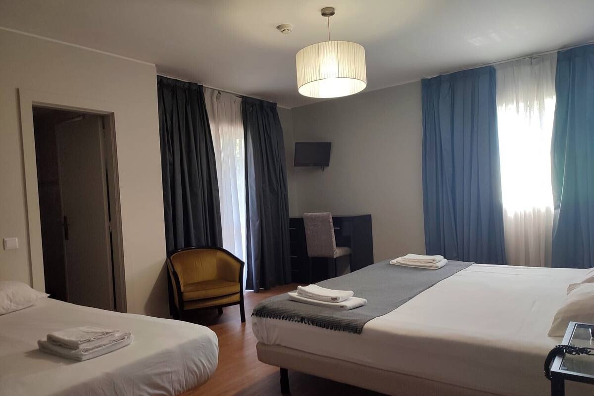 A hotel room with two beds, a desk, a chair, and a TV.