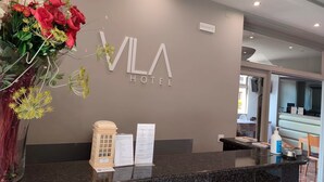 En receptionsdisk med en skylt som visar texten ”VLA HOTEL” och en stor blomsterdekoration.
