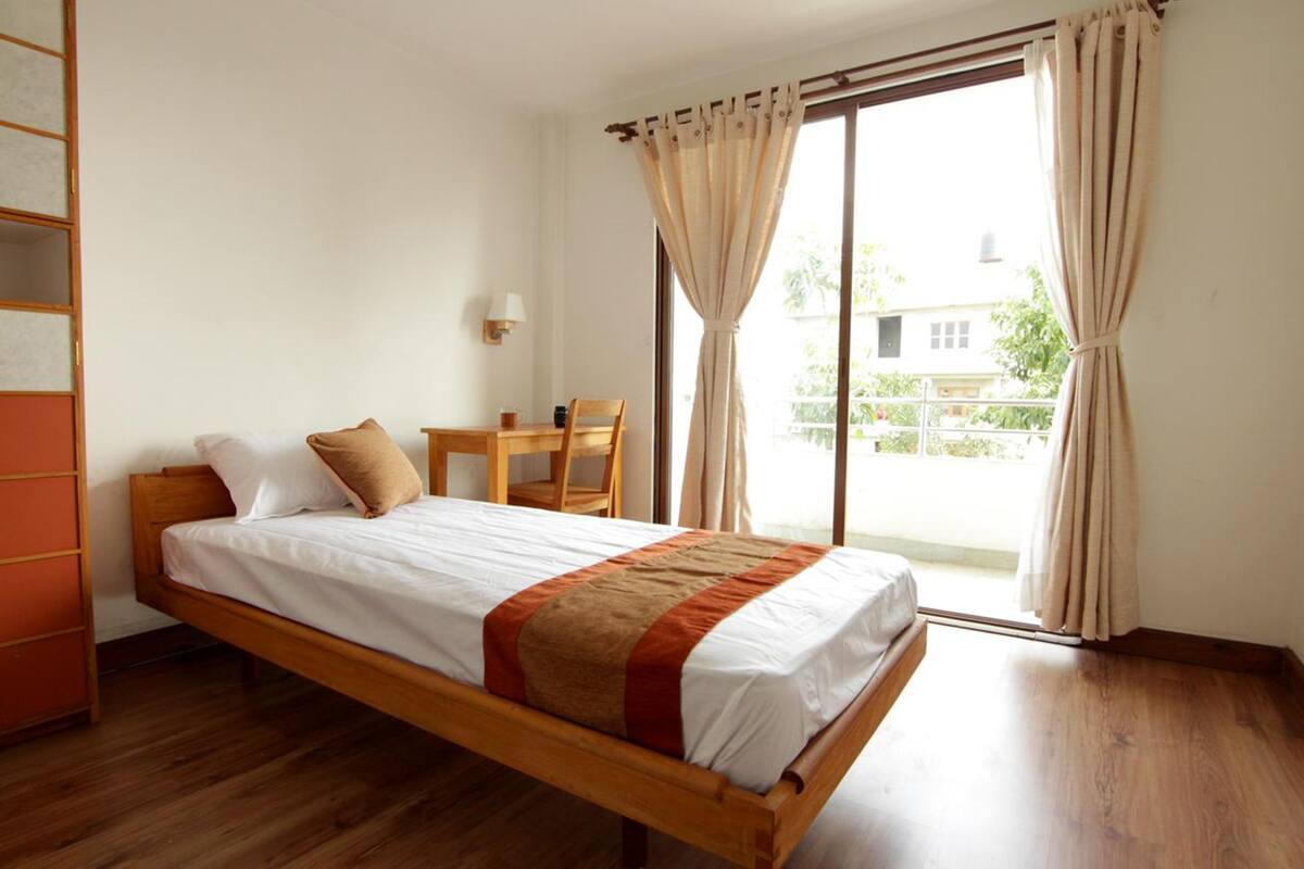 A single bed with a wooden frame, a bedside table, a chair, and a window with curtains.
