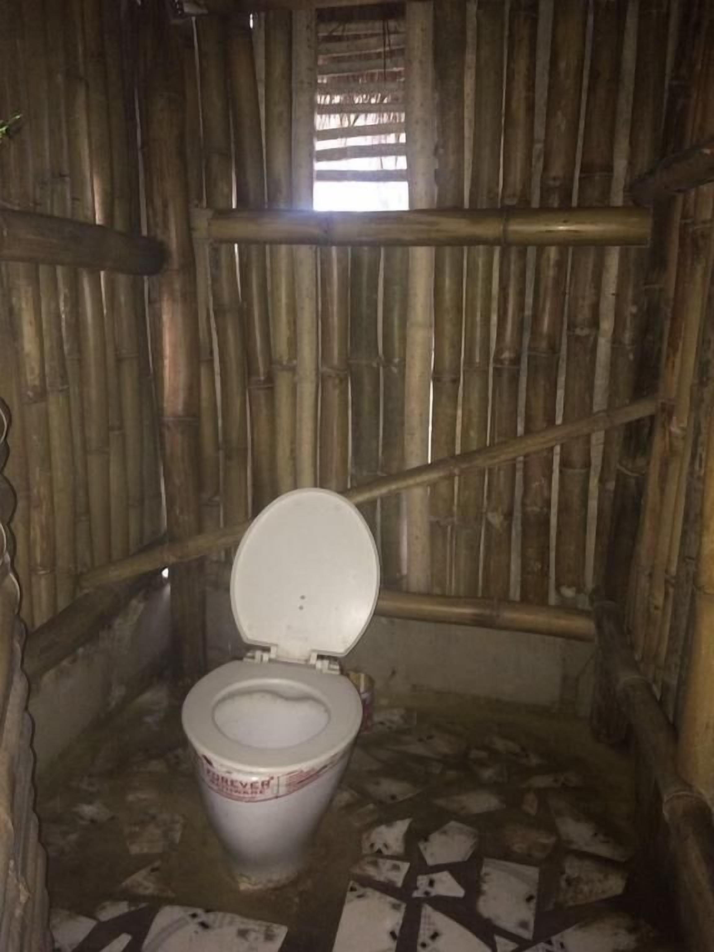 A small, rustic bathroom with a bamboo wall, a single toilet, and a tiled floor.