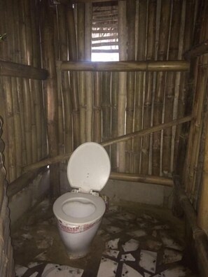 A small, rustic bathroom with a bamboo wall, a single toilet, and a tiled floor. - Natural Bamboo Village (Cape Coast)