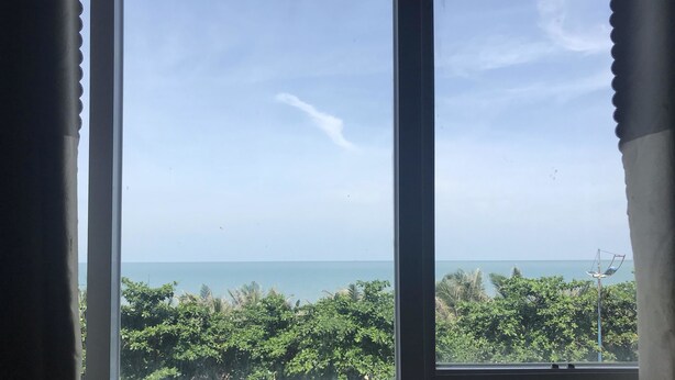 A window with a view of a beach, palm trees, and a clear sky. - Golden Hotel Vung Tau (Ho Chi Minh City)