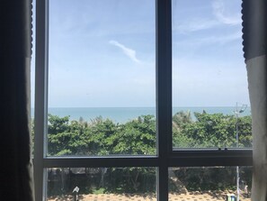 A window with a view of a beach, palm trees, and a clear sky. - Golden Hotel Vung Tau (Ho Chi Minh City)