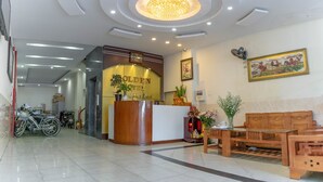 A hotel reception area with a wooden reception desk, a seating area with a sofa and a table, and a ceiling with recessed lighting. - Golden Hotel Vung Tau (Ho Chi Minh City)