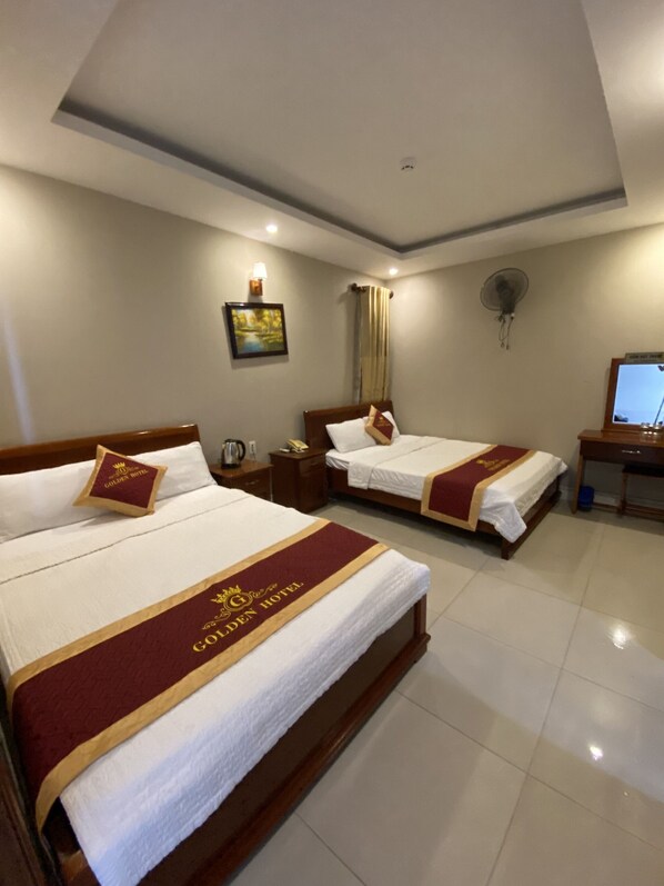 A hotel room with two beds, each with a red and gold bedspread, a nightstand, a lamp, a picture on the wall, and a ceiling fan. - Golden Hotel Vung Tau (Ho Chi Minh City)