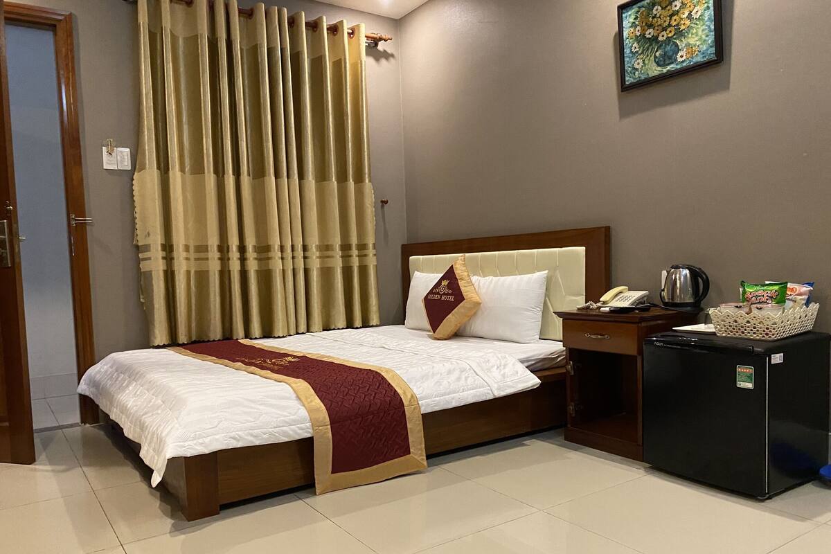 Une chambre d’hôtel avec un lit, une table de chevet, un réfrigérateur, une machine à café et un tableau au mur.