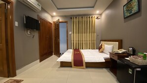 A hotel room with a large bed, a desk with a kettle, a refrigerator, and a TV mounted on the wall. - Golden Hotel Vung Tau (Ho Chi Minh City)