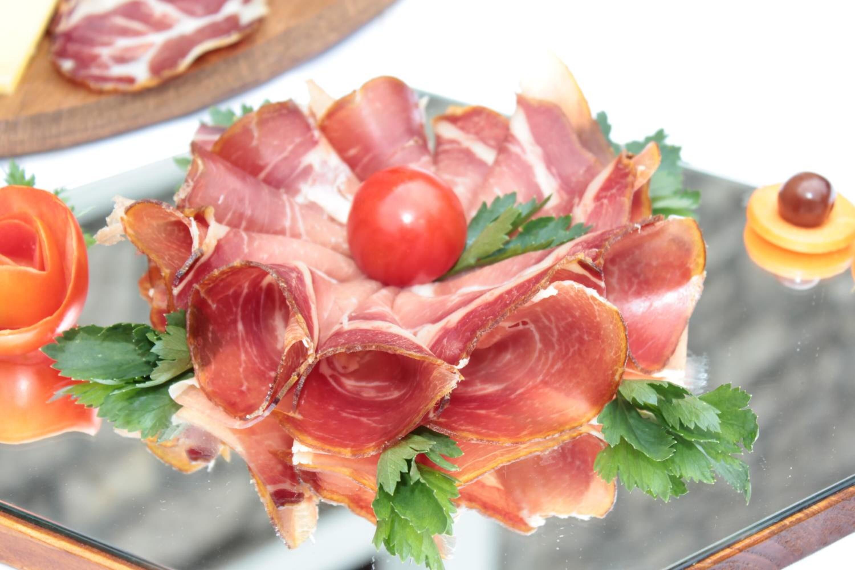 A glass table with a plate of prosciutto, a cherry tomato, and a small fruit.