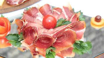 A glass table with a plate of prosciutto, a cherry tomato, and a small fruit.