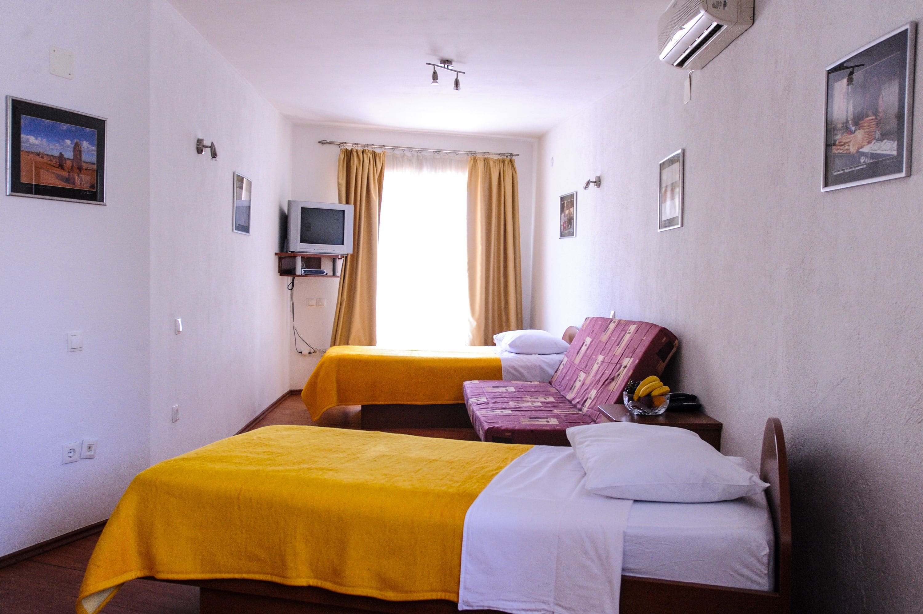Camera d'albergo con due letti, una televisione e una finestra con tende.