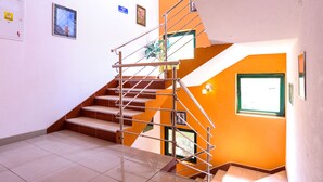 Eine Treppe mit Metallgeländern und Fliesenboden, die zu einem Raum mit orangefarbenen Wänden und einem Fenster führt.