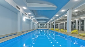 Une piscine intérieure à l’eau d’un bleu cristallin, avec des murs blancs et des chaises longues jaunes.