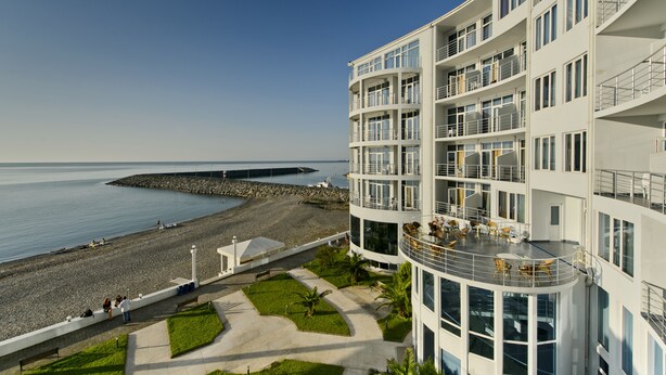 Un hôtel à plusieurs étages doté de balcons donnant sur une plage et la mer.