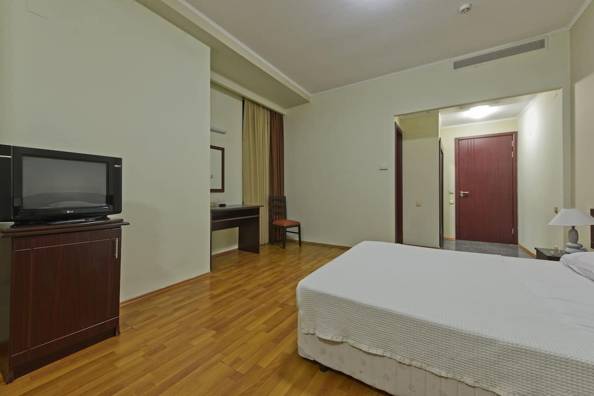 A hotel room with a bed, a desk with a chair, a television, and a wardrobe.