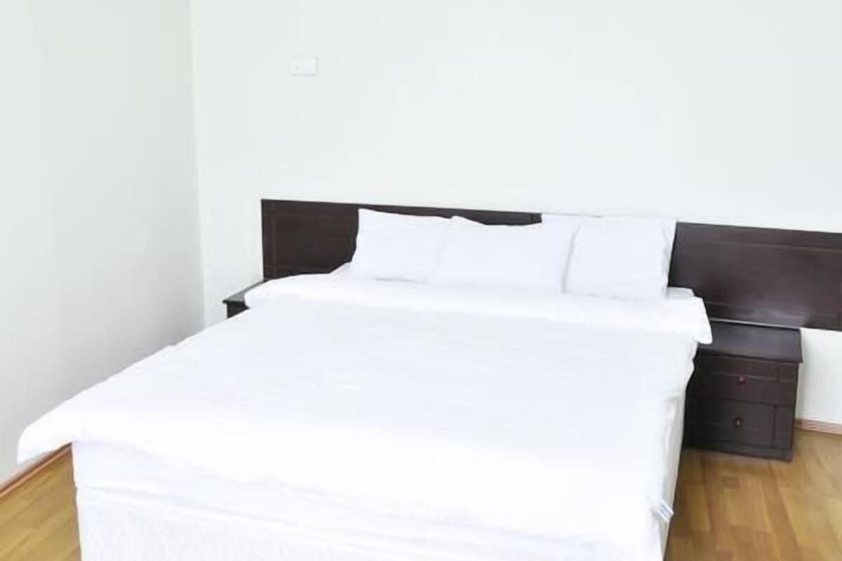 A neatly made bed in a room with a wooden floor and white walls.