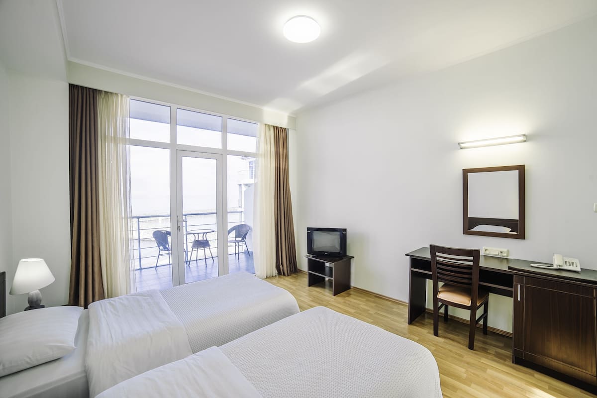A hotel room with two beds, a desk with a chair, a television, and a balcony with chairs.