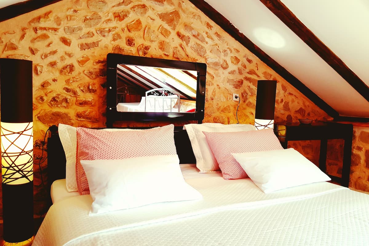 A bedroom with a stone wall, a bed with white bedding, and a mounted TV.