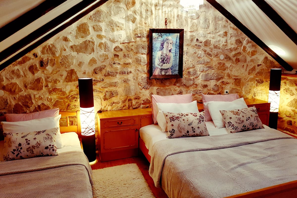A cozy attic bedroom with a stone wall, a framed picture, and two bedside tables with lamps.