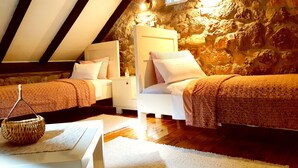 Une chambre mansardée chaleureuse, avec deux lits, un mur en pierre et un plafond en pente.