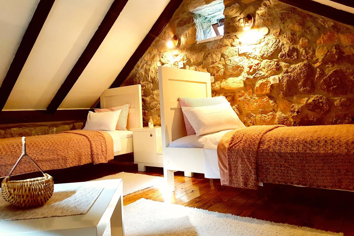 A cozy attic bedroom with two beds, a stone wall, and a sloped ceiling.