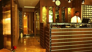 Zona de recepción de un hotel con un mostrador de madera, un reloj y una escalera con escalones de mármol.