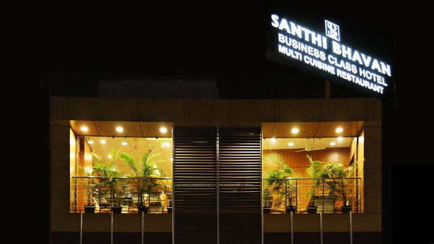 Exterior del Hotel Santhi Bhavan Business Class, con un cartel llamativo y una entrada con alfombra roja.