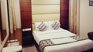 Habitación de hotel con cama, cabecero de madera, cortinas, ventilador de techo y aire acondicionado.