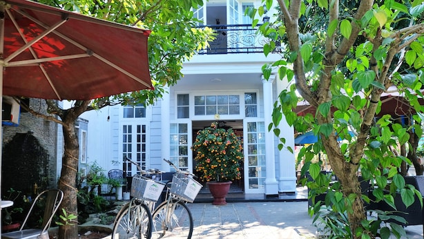 A bicycle parked in front of a building with a large potted plant and a red umbrella. - Cochi Villa Hoi An (Da Nang)