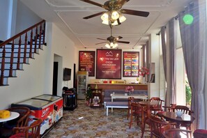 A hotel lobby with a staircase, reception desk, dining area, and a ceiling fan. - Cochi Villa Hoi An (Da Nang)