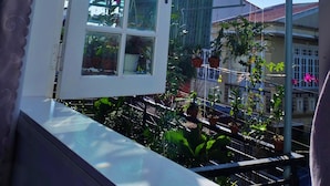 A window with a view of a balcony garden, a pergola, and a building in the background. - Cochi Villa Hoi An (Da Nang)