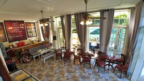A hotel lobby with a patterned floor, seating area with tables and chairs, a sofa, a reception desk, and a large window with curtains. - Cochi Villa Hoi An (Da Nang)