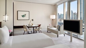A hotel room with a large bed, a desk with chairs, a TV, and a city view.
