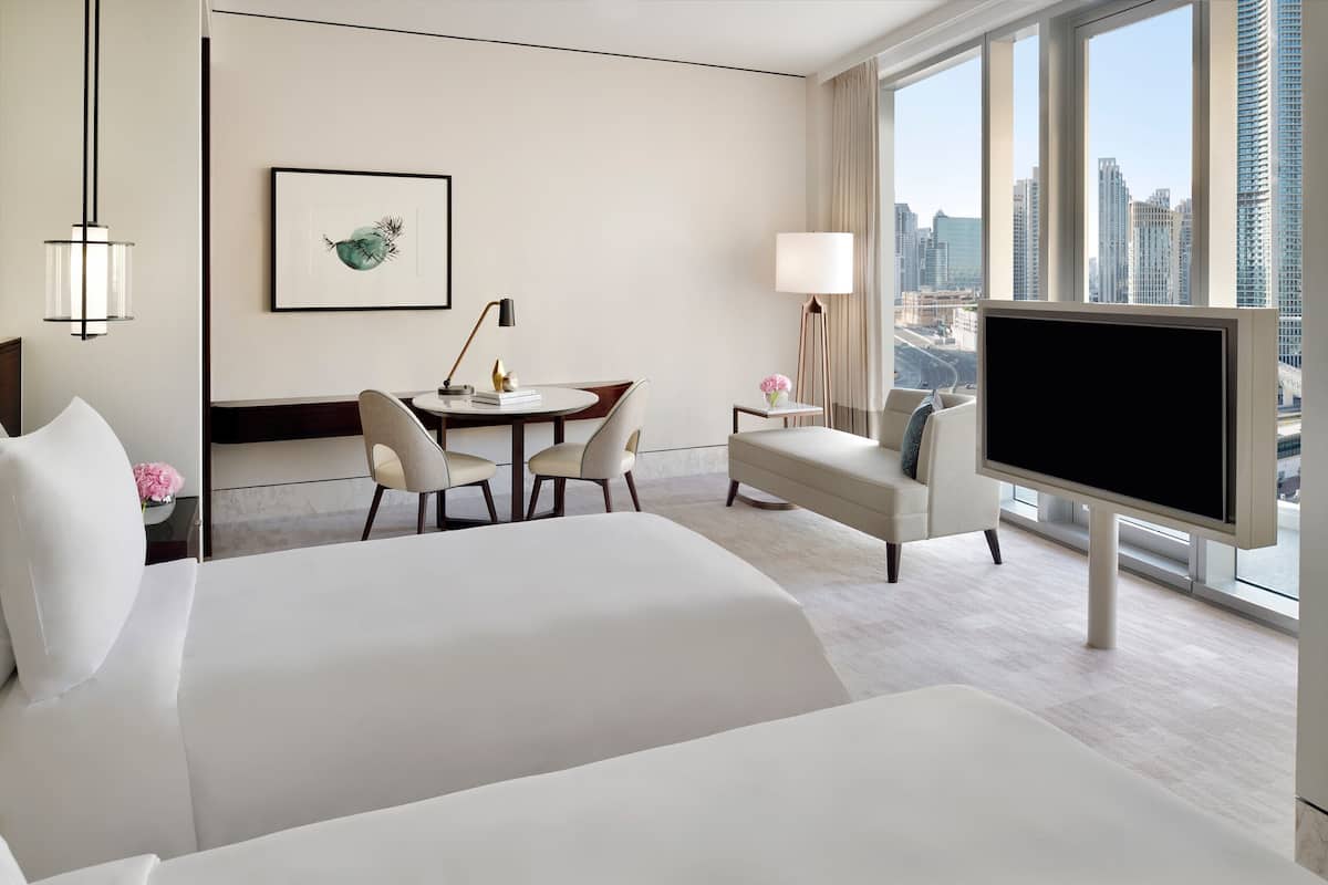 A hotel room with a large bed, a desk with chairs, a TV, and a city view.