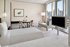 A hotel room with a large bed, a desk with chairs, a TV, and a city view.