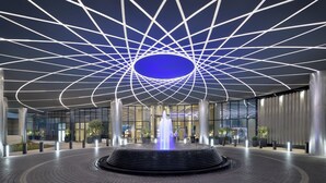 A modern building entrance with a geometric ceiling design, a central fountain, and a paved walkway.