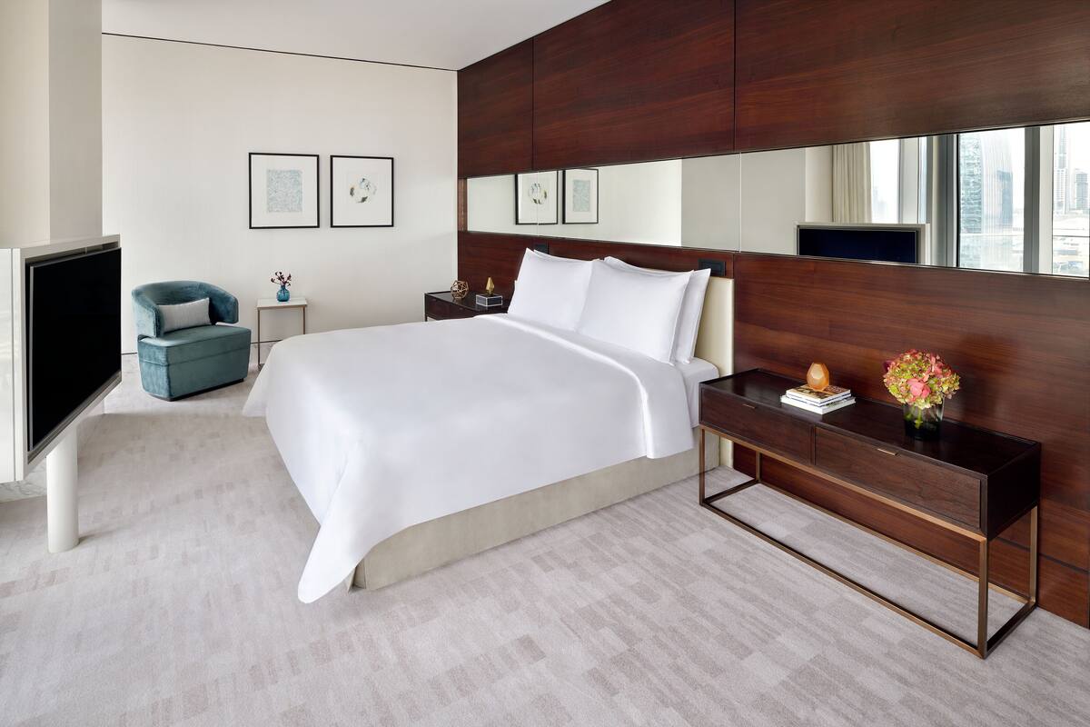 A modern hotel room with a large bed, a TV, a desk, and a city view.