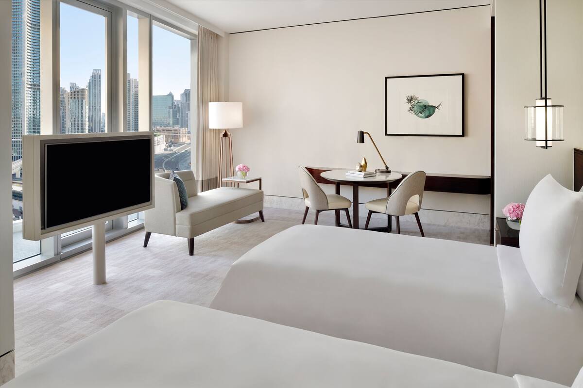 A hotel room with a large bed, a TV, a desk with chairs, a lamp, and a framed picture on the wall.