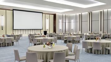 A large conference room with multiple round tables, chairs, and a large screen.