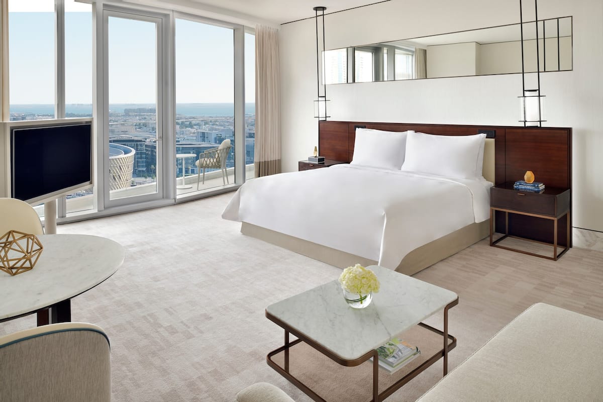 A modern hotel room with a large bed, a TV, a small table with a vase, and a city view.