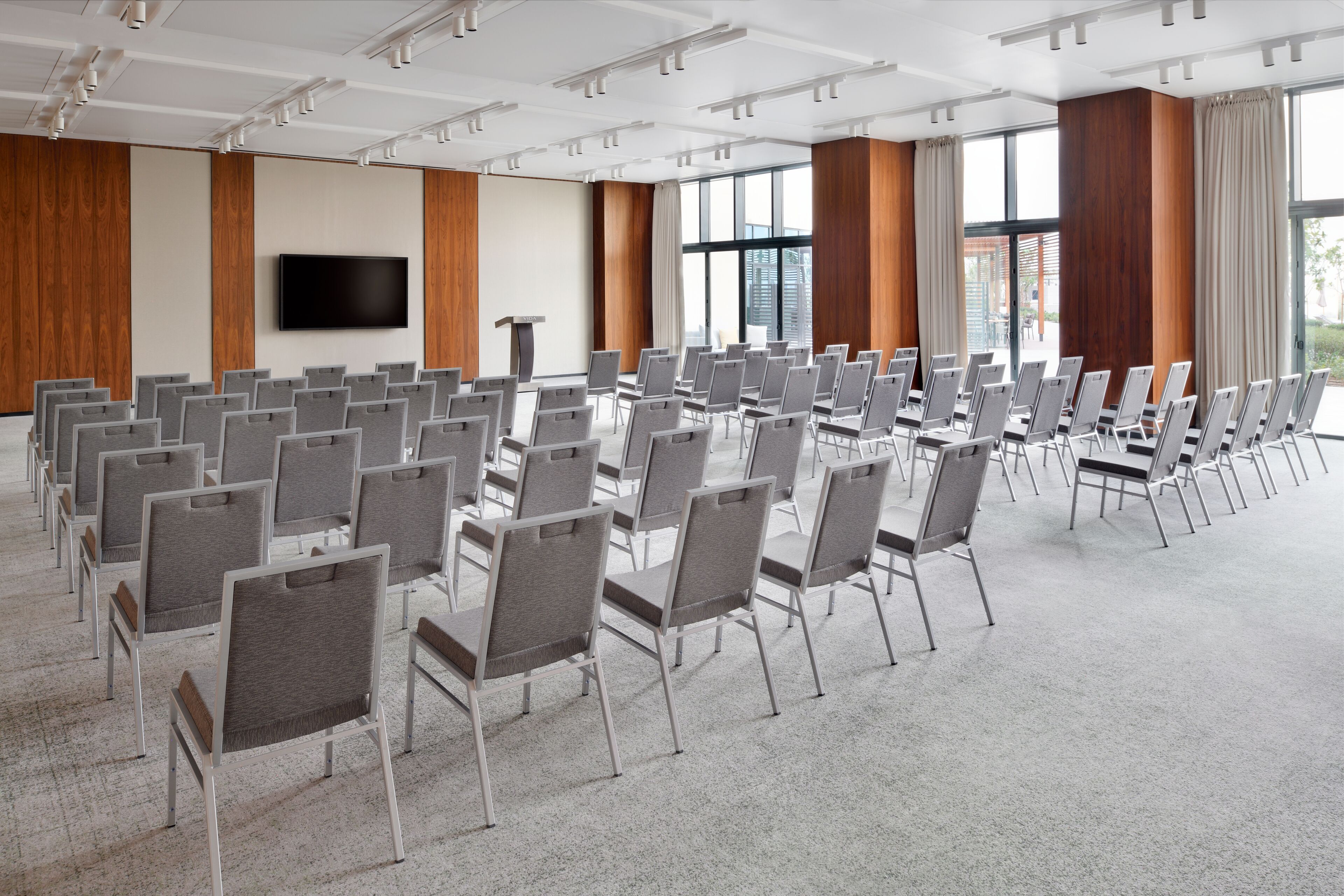 Un salón de conferencias con filas de sillas, un televisor de pantalla plana grande y paneles de madera en las paredes.