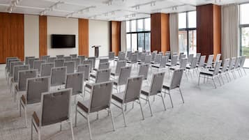 Une salle de conférence avec des rangées de chaises, un grand téléviseur à écran plat et des panneaux de bois aux murs.