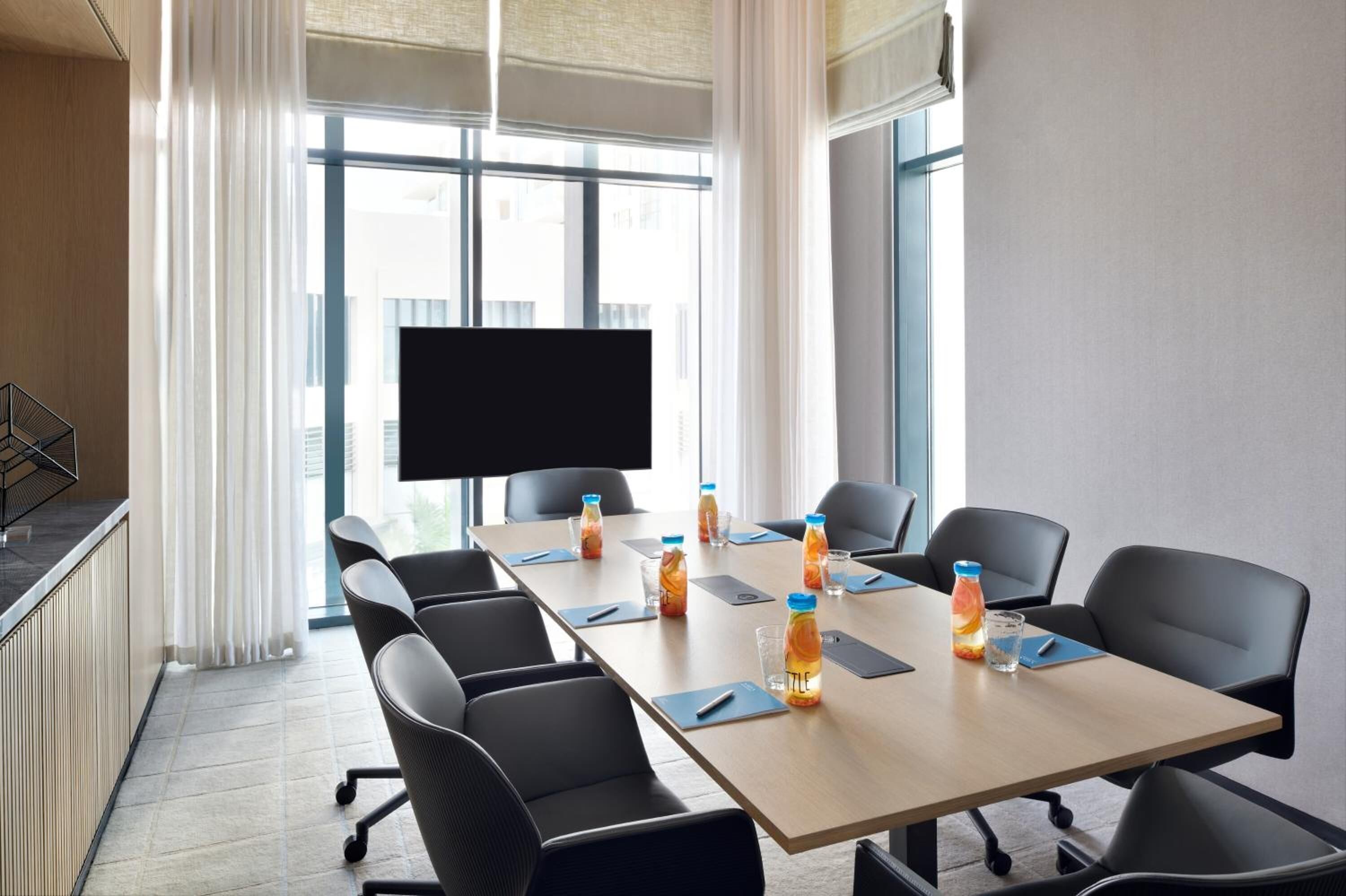 A conference room with a long table, black chairs, and a flat-screen TV.
