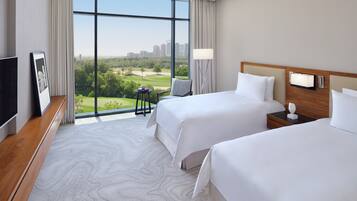 Ein Hotelzimmer mit zwei Betten, einem Fernseher, einem Schreibtisch und einem großen Fenster mit Blick auf einen Golfplatz und die Stadtlandschaft.