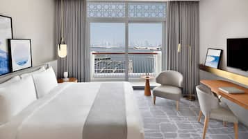 Habitación de hotel con una cama grande, un escritorio, una silla, un televisor y vistas de la silueta urbana a través de una ventana.