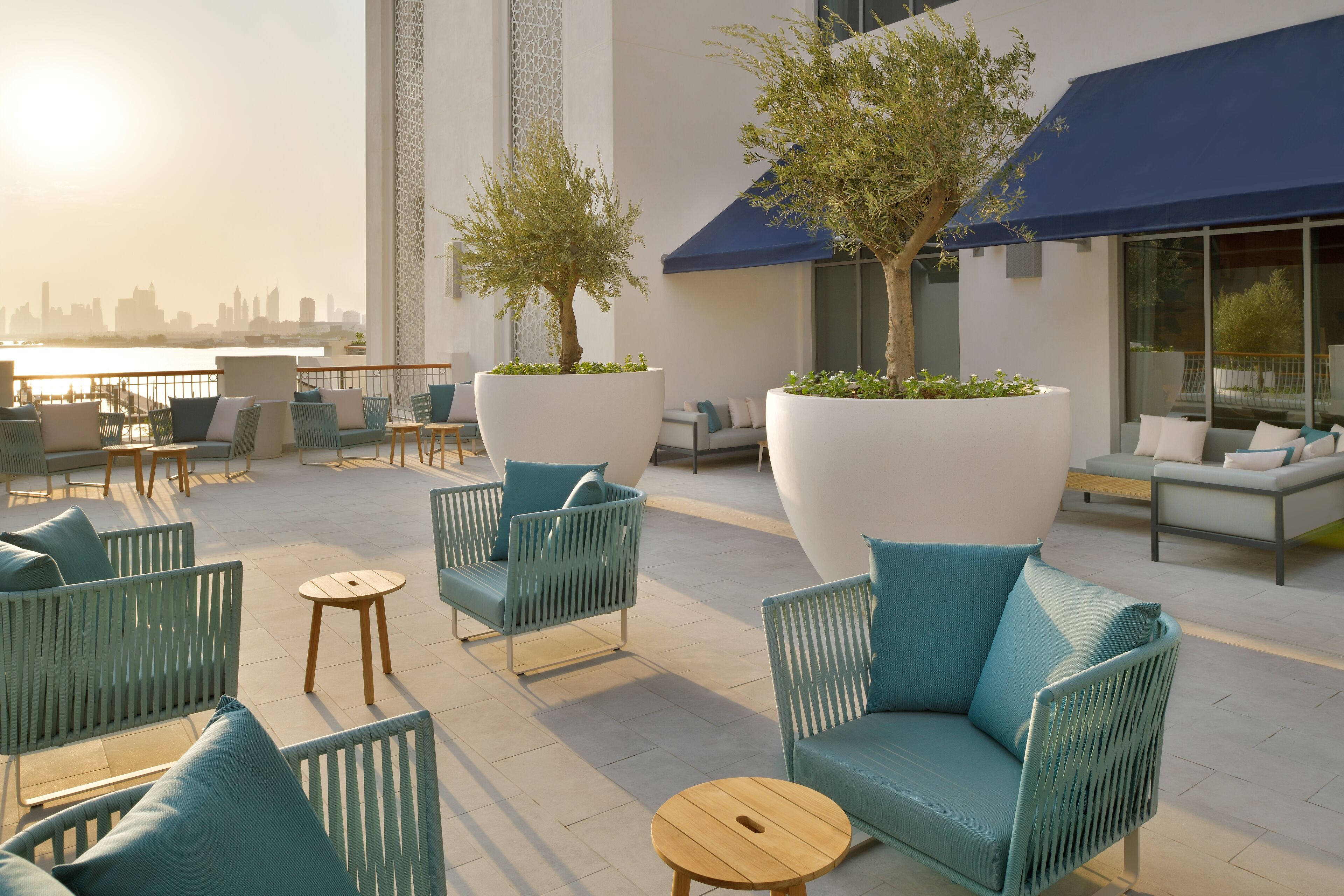 Un área de estar al aire libre con muebles modernos y grandes macetas, con vista a un paisaje urbano.