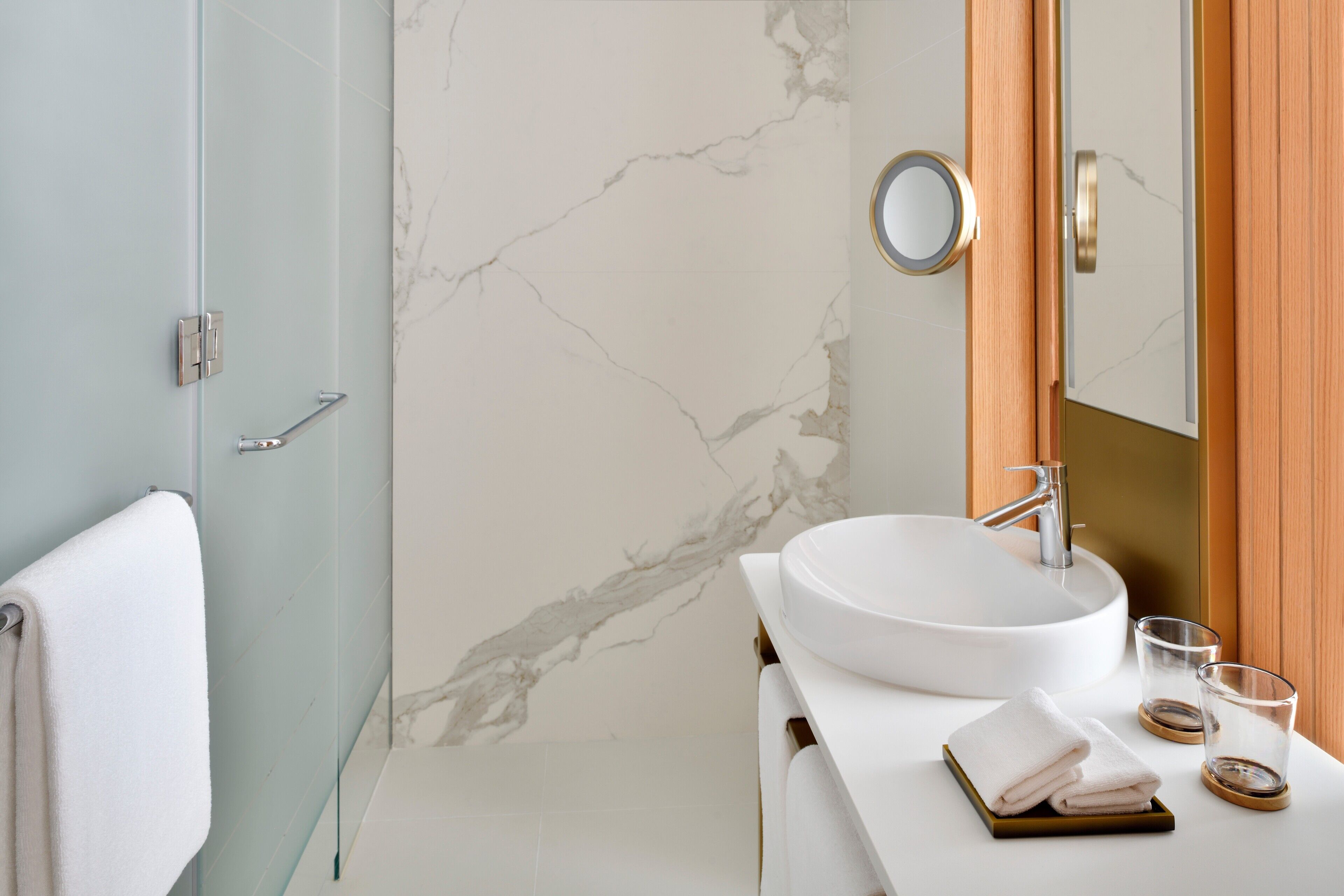 A bathroom with a marble wall, a white sink, a towel, and a glass.