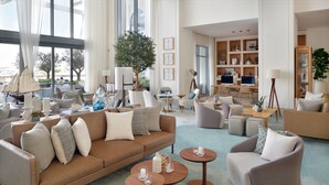 A spacious living room with a large window, a sofa set, a coffee table, and a desk area with a computer. - Vida Creek Harbour (Dubai)