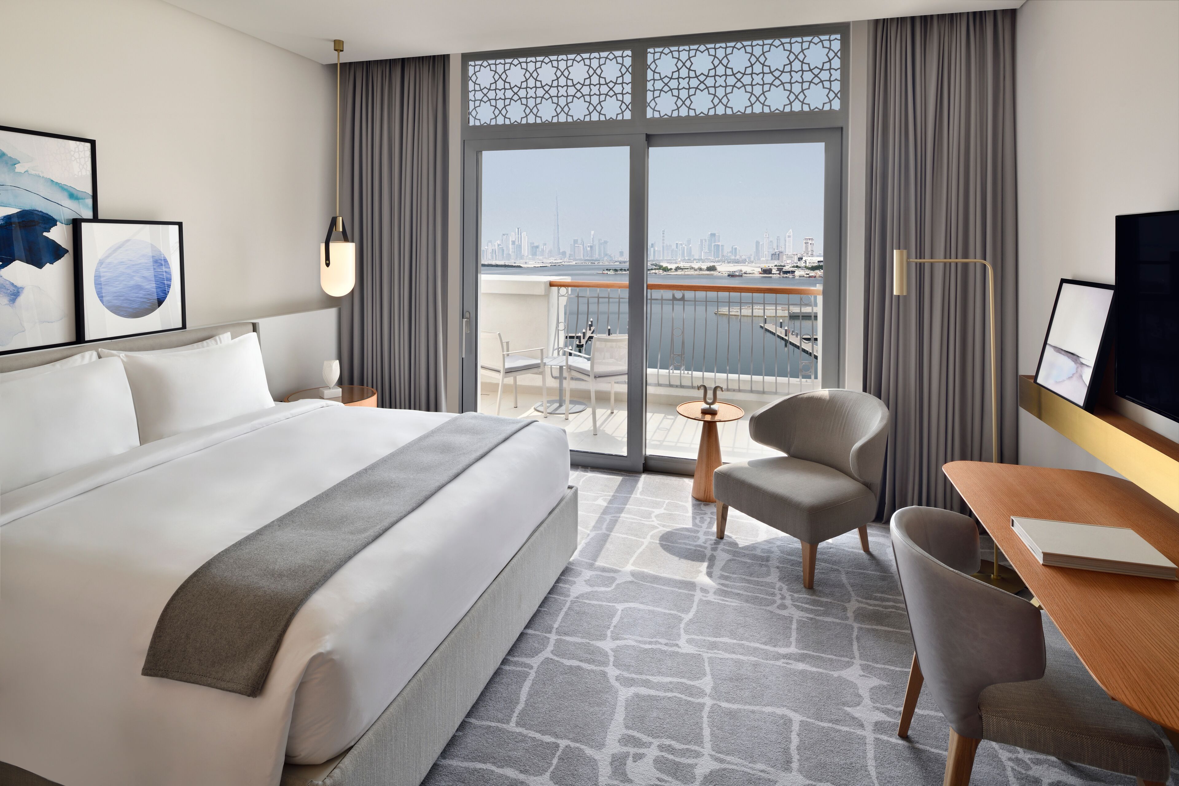 Une chambre d’hôtel avec un grand lit, un bureau, une chaise et une vue sur la ville par une grande fenêtre.