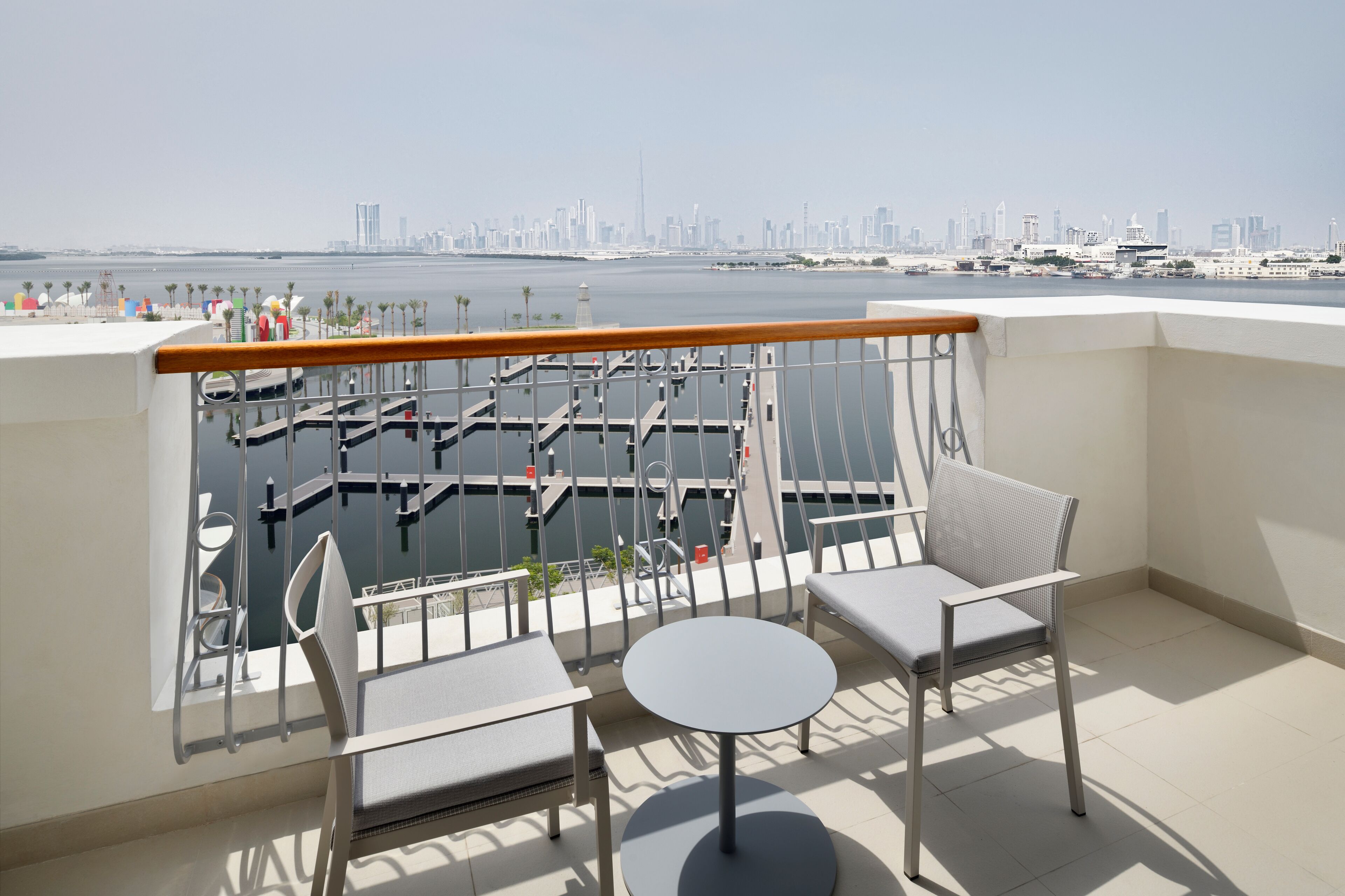 A balcony with two chairs and a table, overlooking a marina and a city skyline.