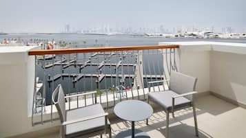 Un balcón con dos sillas y una mesa, con vistas a un puerto deportivo y al horizonte de la ciudad.